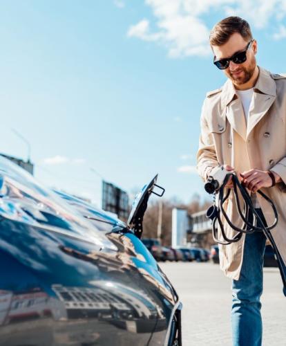 Man holds charging cable in front of EV bonnet